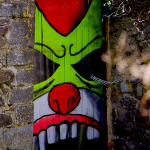 Porte en bois recouverte d'une peitnure représentant un visage vert et entourée de murs en pierre - Belgique  - collection de photos clin d'oeil, catégorie portes